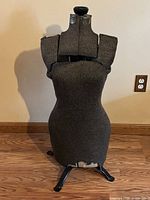Front view of brown fabric dress form on stand showing overall shape and tear at hem