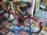 Full side view of the candy red electric bicycle with battery, rear rack and basket visible