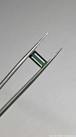 Green baguette-cut tourmaline held in tweezers, showing color and cut