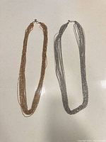 Gold-tone and silver-tone multi-strand necklaces side by side, full view