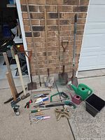 Overview of all long-handled and hand tools against wall and on driveway