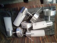 Six cylindrical wall sconces piled on striped surface, brushed nickel bases, white glass shades, loose wiring visible
