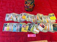 Spread of large quantity of assorted Pokémon cards with collector tin visible