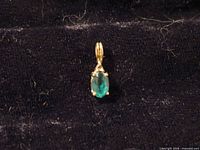 Front view of gold pendant showing green gemstone and prong setting