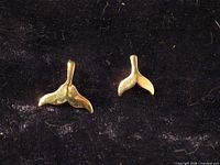 Front view of both gold whale tail pendants on dark fabric