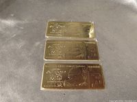 Three gold tone replica bars in sleeves, front designs visible