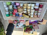 Clear bin filled with assorted ribbon spools, black cylindrical boxes and loose ribbons