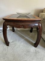 Angled view of wooden end table showing legs, apron, glass panel, leaf bowl