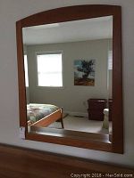 Full view of rectangular wall mirror showing curved top and cherry stained wood frame in bedroom setting.