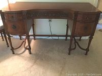 Front view of antique tiger maple desk or vanity showing its curved front, central and side drawers, and carved details on legs and skirt.