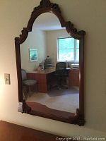 Full view of the large antique wall mirror hanging on a wall, showing its rectangular shape with arched top and visible reflection of room.