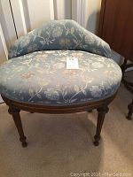 Front view of vanity stool upholstered with Wedgwood blue floral fabric showing round seat and low curved backrest.