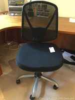 Front view of black office chair featuring padded seat and elastic mesh back, on five-legged rolling base.