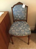Full front view of chair showing wood frame and upholstered fabric back and seat with floral motif