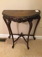 Front view of a dark stained antique demilune table showing ornate apron and curved legs