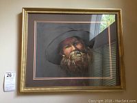 Framed original portrait of bearded man in a hat by Dodie Holland, showing full frame and wall reflection.