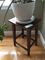 Full view of the dark wood stool or plant stand with a white pot on top, showing its overall shape and size.