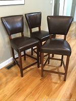 Three dark brown faux leather bar stools arranged together