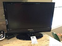 Samsung 19-inch flat panel TV shown on countertop with remote visible, showcasing its black screen and brand logo.