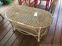 Full side view of the oval wicker coffee table showing its structure, weaving and rattan-style legs.