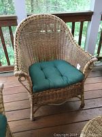 Front and partial side view of armchair showing natural wicker weave and dark green cushion on wooden deck.
