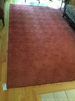 Full view of poppy red wool area rug laid on hardwood floor showing overall condition and size