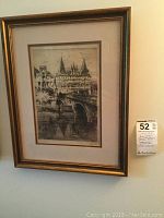 Framed print hanging on wall with visible details of the Holstentor structure, bridge, and water beneath, framed in gold-tone frame with double mat.