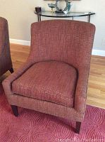 Front view of red upholstered arm chair with textured fabric and walnut legs on a red rug.