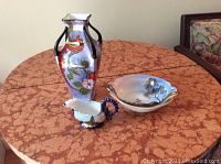 Three porcelain pieces: Noritake vase, Noritake bowl, miniature Dresden gravy boat on round table