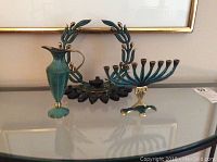 Photo showing small menorah, larger menorah, and decorative pitcher on a glass shelf.