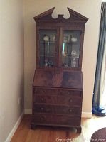 Front view of wood secretary desk with glass enclosed shelves on top and drawers below.