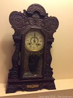 Front view of the New Haven mantel clock showing carved wooden case and glass panel with decorative gold pattern.