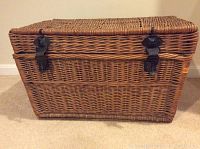 Front view of the rectangular wicker trunk showing two black metal clasps, tightly woven wicker in natural brown.