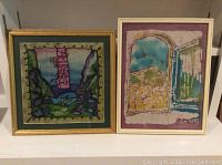 Two framed batiks side by side, one with landscape through window and the other depicting Jacob sleeping on a rock