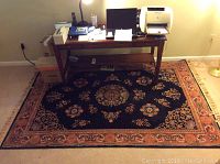 Photo showing the entire rectangular area rug under a desk in a room, highlighting black field with rust and multicolor oriental design.