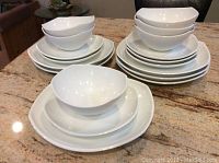 Full view of stacked white Dansk Classic Fjord dinnerware set with dinner plates, salad plates, and soup bowls on granite countertop.