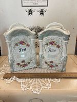 Front view of both porcelain canisters showing labels and ornate design