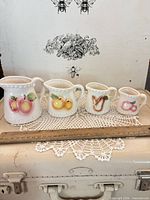 Group shot showing all four porcelain measuring cups with fruit motifs and ruler for scale
