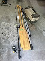 All items laid out: rod with reel, two paddles, two aluminum boat hooks, tackle box closed, metal anchor