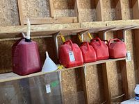 Five red plastic fuel cans with spouts, white funnel, yellow caps on shelf