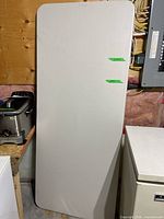 Full view of white plastic folding table standing on edge