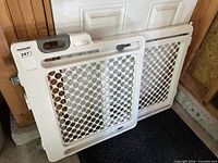 Full view of off-white plastic baby gate, two-panel adjustable design