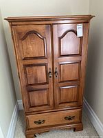 Front view of closed wardrobe showing paneled doors, brass pulls, lower drawer, bracket feet