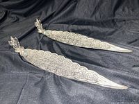 Pair of ornate leaf-shaped metal incense holders on cloth backdrop