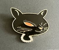 Front view of black enamel cat brooch showing gold tone outline, orange eye accent, rhinestone collar