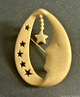 Front view of gold-tone brooch showing moon profile, cut-out stars, dangling star charm