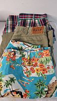Stacked view showing plaid shorts, khaki pants with Polo patch, Hawaiian shorts