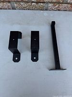 Three black steel brackets laid out on flat surface