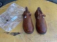 Pair of brown Mary Jane shoes with packaging bag