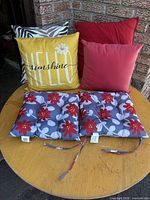 Group image of two seat cushions and three visible pillows showing patterns and colors